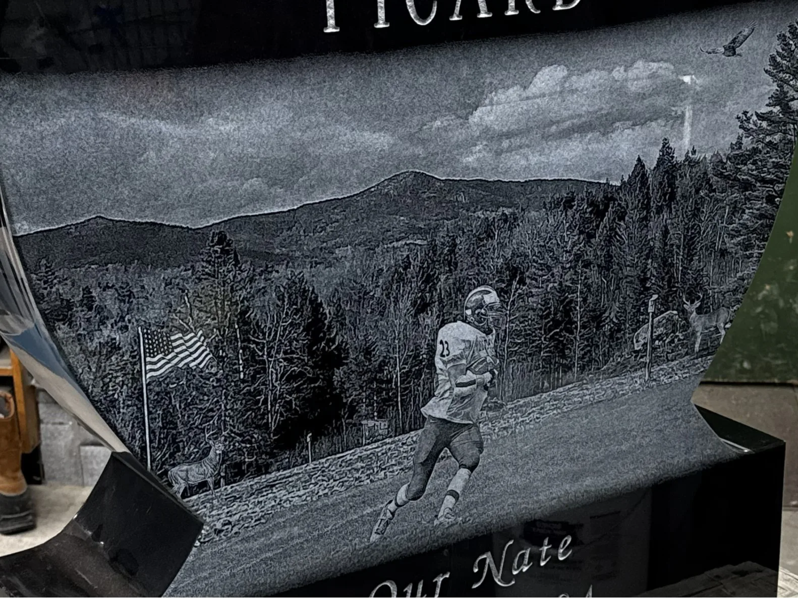 Laser-etched football player and Vermont mountain scene on the Picard memorial — polished black granite