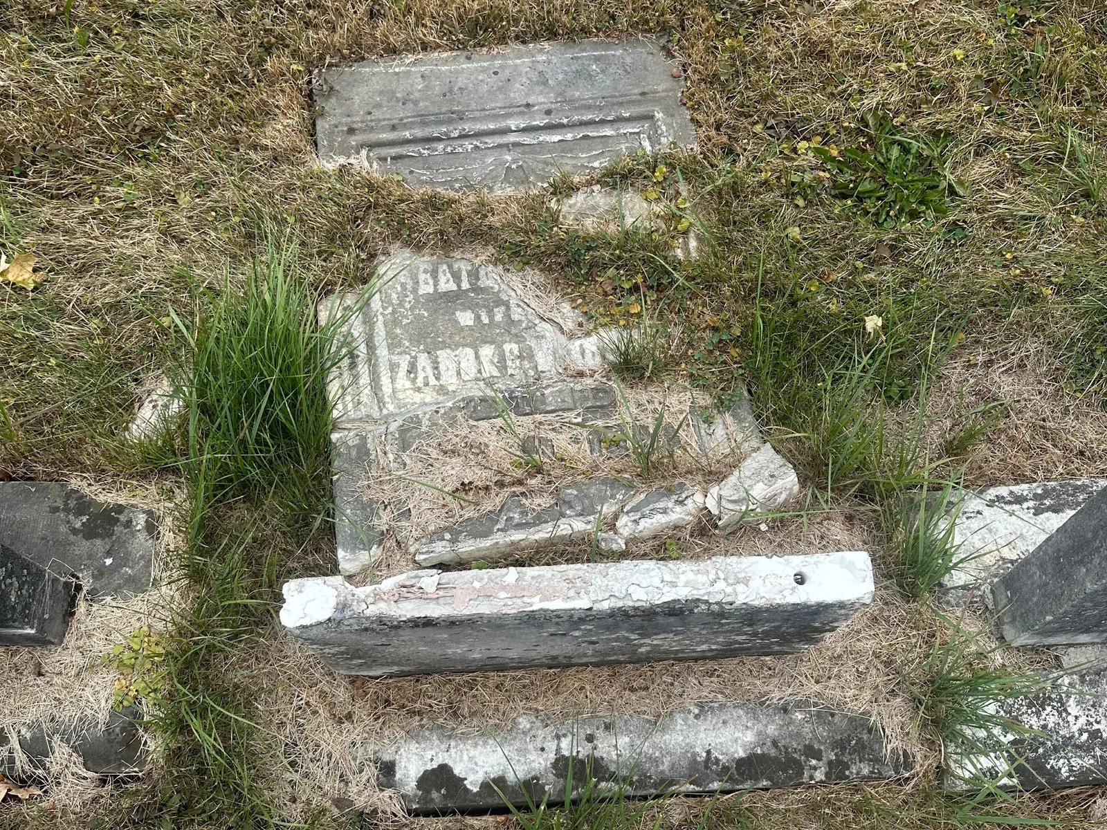 A monument tablet shattered into multiple pieces on the ground, beyond what can be reassembled or restored