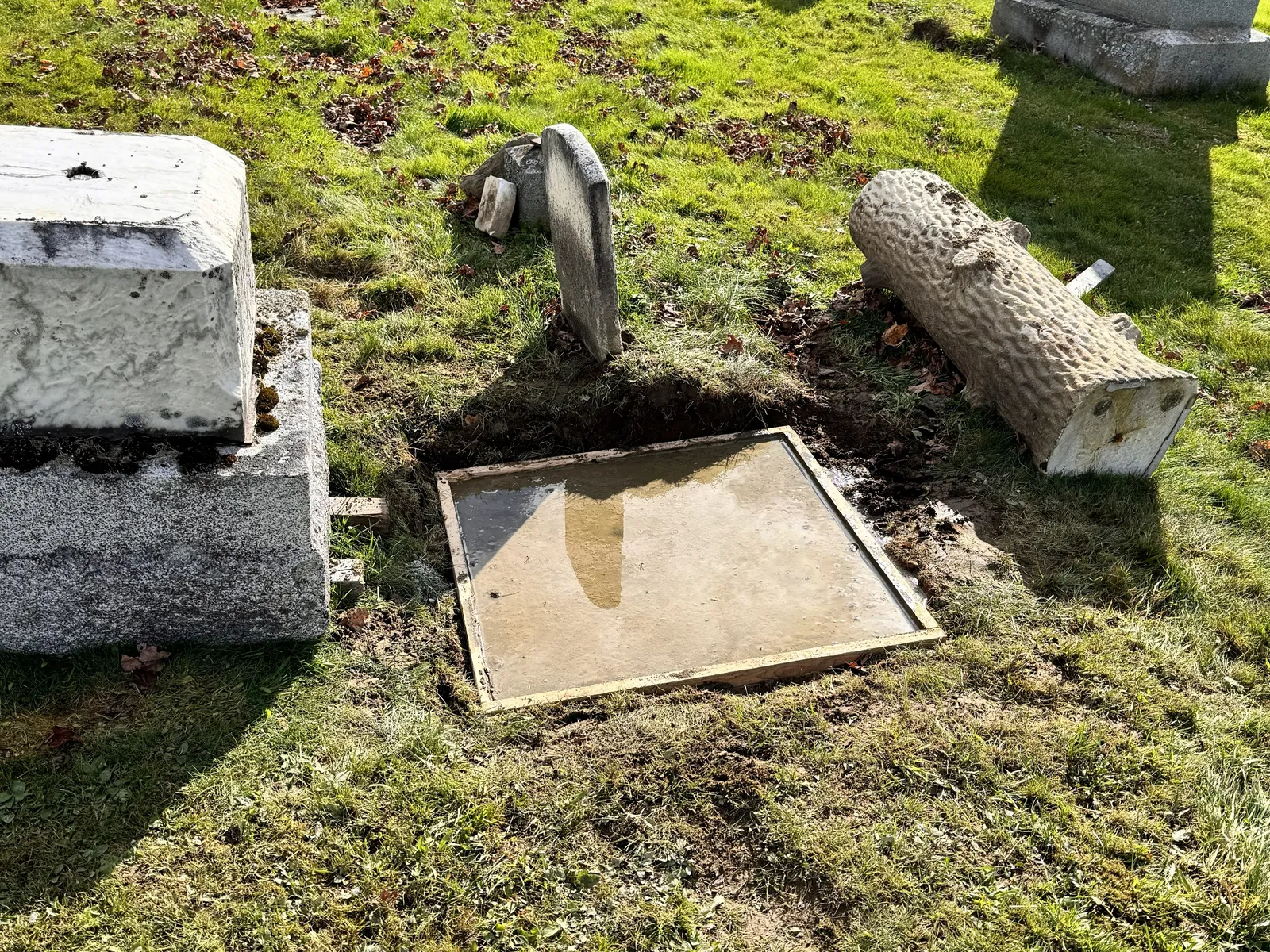 A new poured concrete foundation set in place, with the displaced monument and base pieces it will receive resting alongside it on the lot