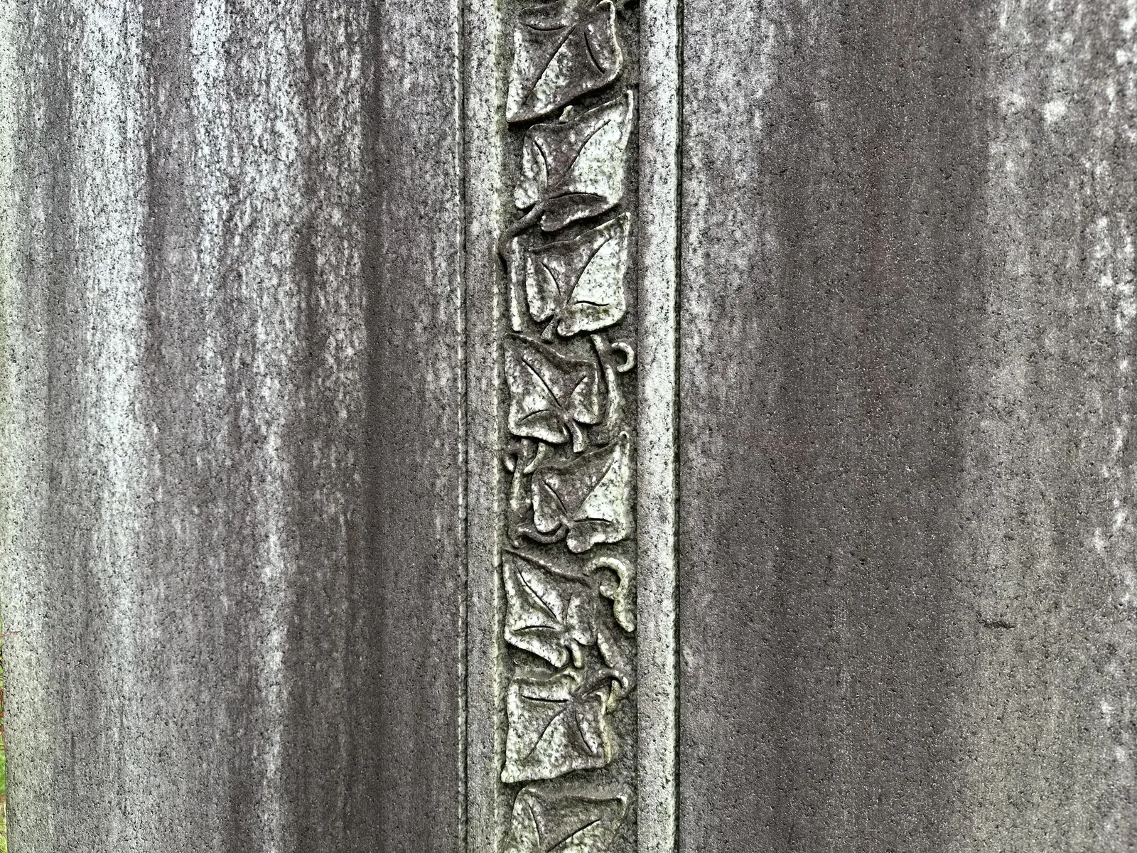Vertical dark atmospheric streaking running down a carved granite headstone, framing a decorative ivy-leaf border