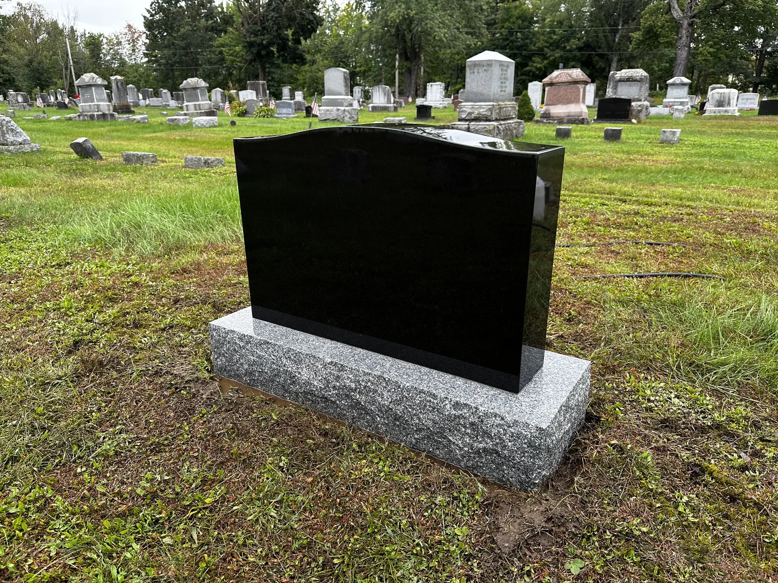 The same round-top granite monument after professional cleaning, with the surface clear and lettering readable