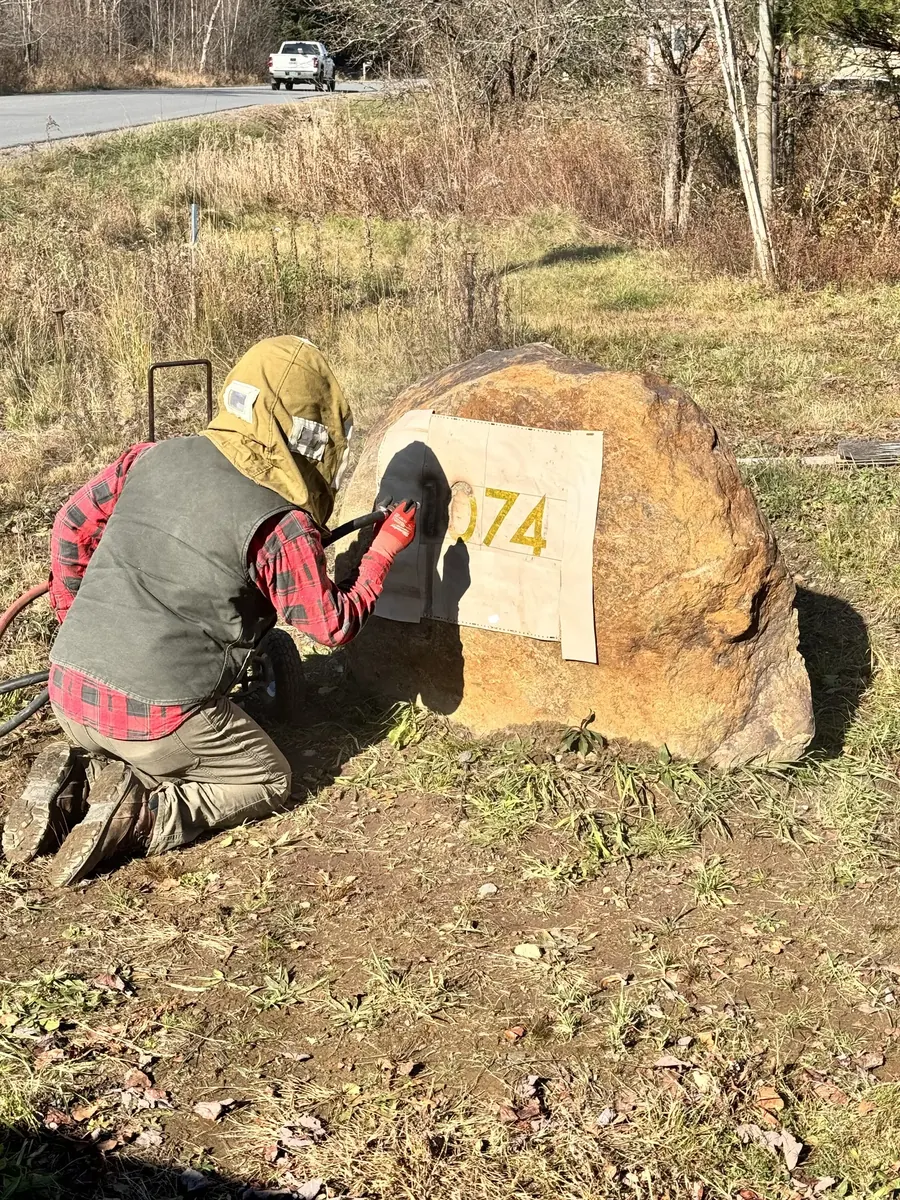 Worker in protective gear sandblasting custom lettering into a granite boulder